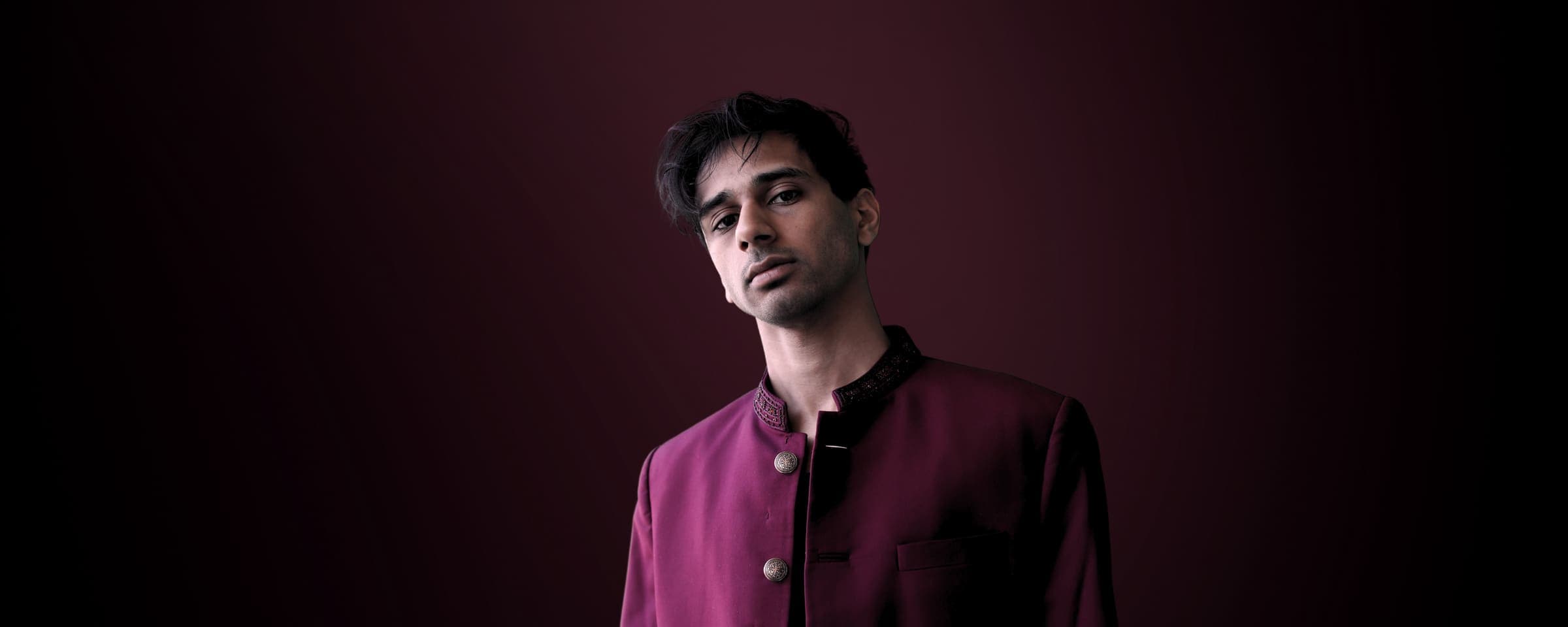 Bisaria, electronic music producer, in a burgundy bandhgala against a deep wine backdrop